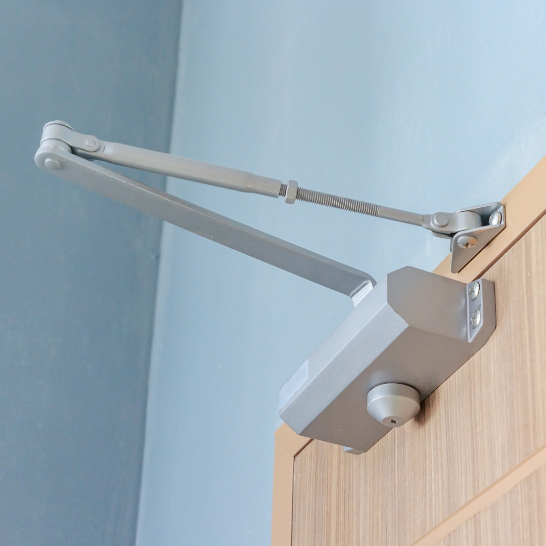 Dispositivo cierra puertas de piso instalado en la base de una puerta de acceso